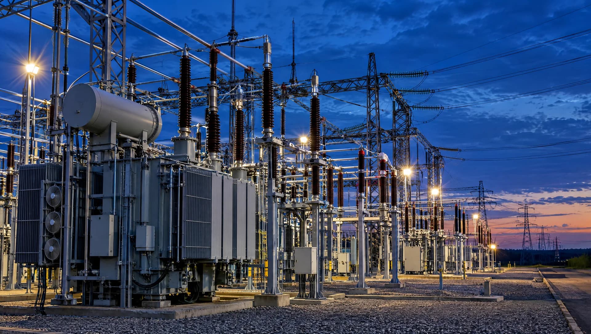 Subestação de alta tensão com transformadores e isoladores ao anoitecer